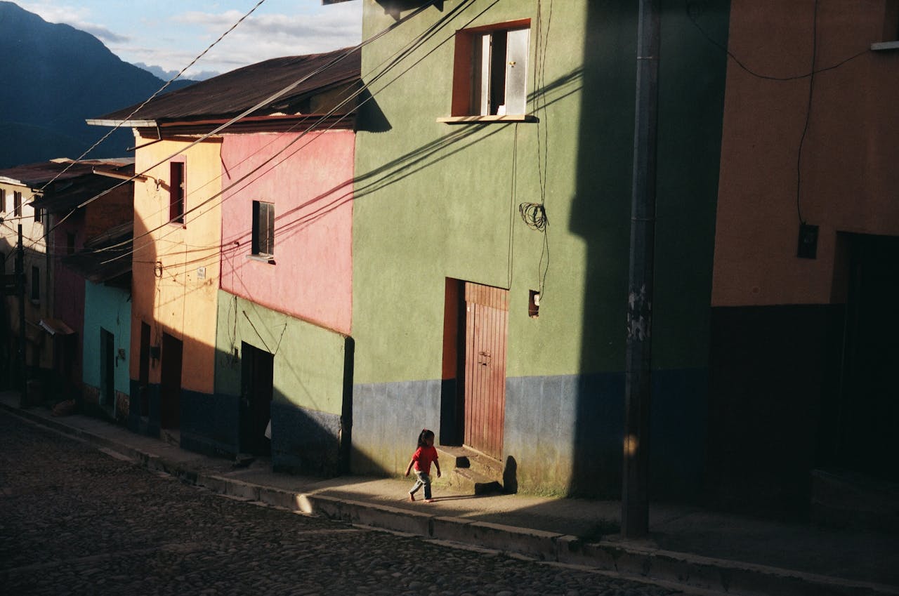A child walks along colorful houses in Coroico, Bolivia, under sunlight.